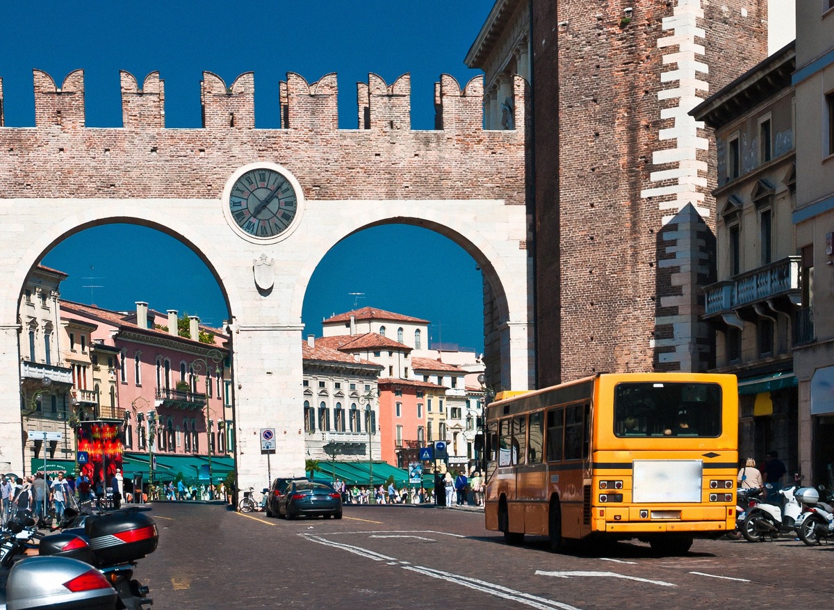 A yellow city bus passing the Portoni della Bra on Piazza Bra in Verona